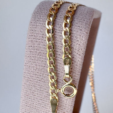 A gold-toned chain necklace with a flat curb link design and a small circular ring charm, draped over a light pink textured jewelry display stand.